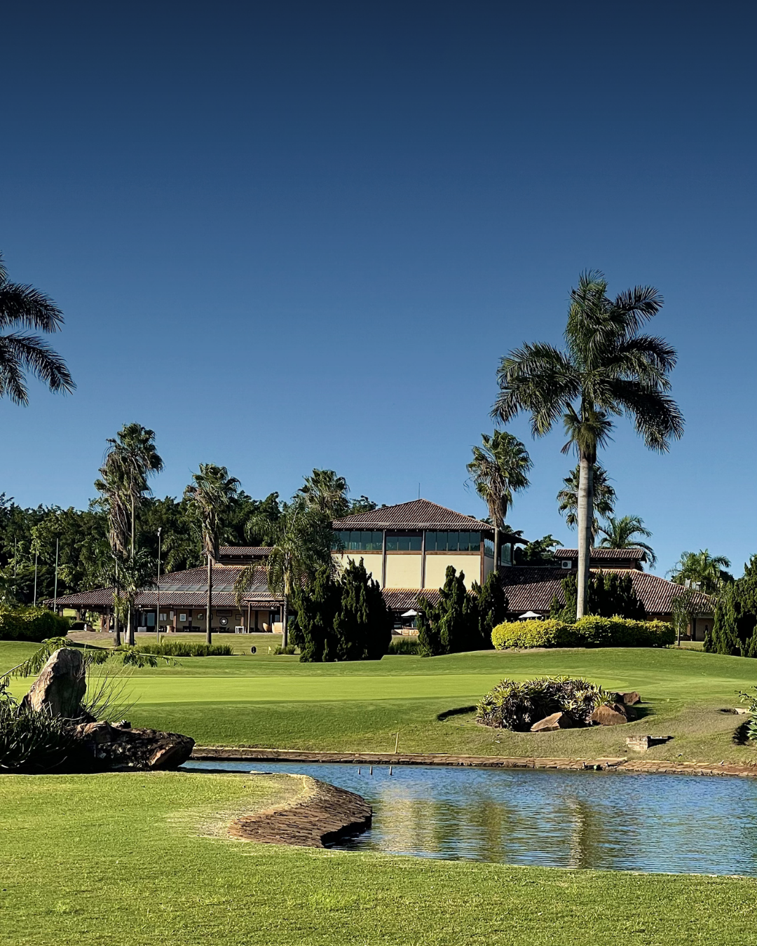 Vista do clubhouse do Damha Golf Club com lago e palmeiras
